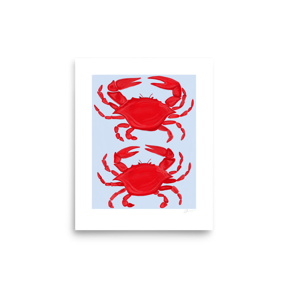 Illustration of two bright red crabs positioned in a mirrored fashion on a light blue background, printed on matte paper. The crabs have detailed claws and legs, with a smooth texture that contrasts with the soft finish of the paper.